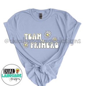 Peut inclure: T-shirt bleu clair avec le texte "TEAM PRIMERO" dans une police rétro avec des marguerites jaunes autour du texte.