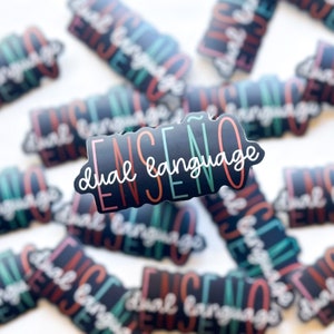 May include: A black sticker with the text "ENSEÑO dual language" in colorful lettering. The sticker is surrounded by other stickers with similar designs.