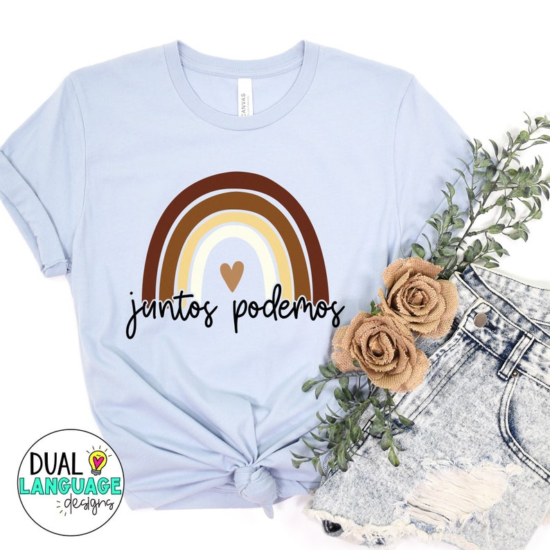 Peut inclure: Un t-shirt bleu clair avec un motif arc-en-ciel et le texte "juntos podemos" en noir. L'arc-en-ciel est compos&eacute; de bandes brunes, beiges et blanches. Un petit c&oelig;ur se trouve au centre de l'arc-en-ciel.