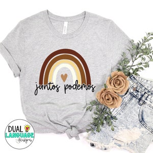 Peut inclure: Un t-shirt gris avec un motif arc-en-ciel dans des tons de brun, beige et blanc. L'arc-en-ciel a un petit c&oelig;ur au centre. Le texte "juntos podemos" est &eacute;crit en noir sous l'arc-en-ciel.
