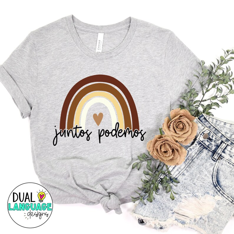 Peut inclure: Un t-shirt gris avec un motif arc-en-ciel dans des tons de brun, beige et blanc. L'arc-en-ciel a un petit c&oelig;ur au centre. Le texte "juntos podemos" est &eacute;crit en noir sous l'arc-en-ciel.