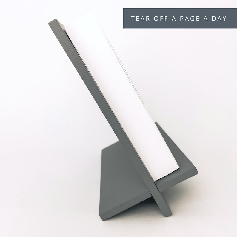 May include: A gray, angled desk calendar with a stack of white pages. The calendar is supported by a gray stand. The text "TEAR OFF A PAGE A DAY" is displayed at the top.