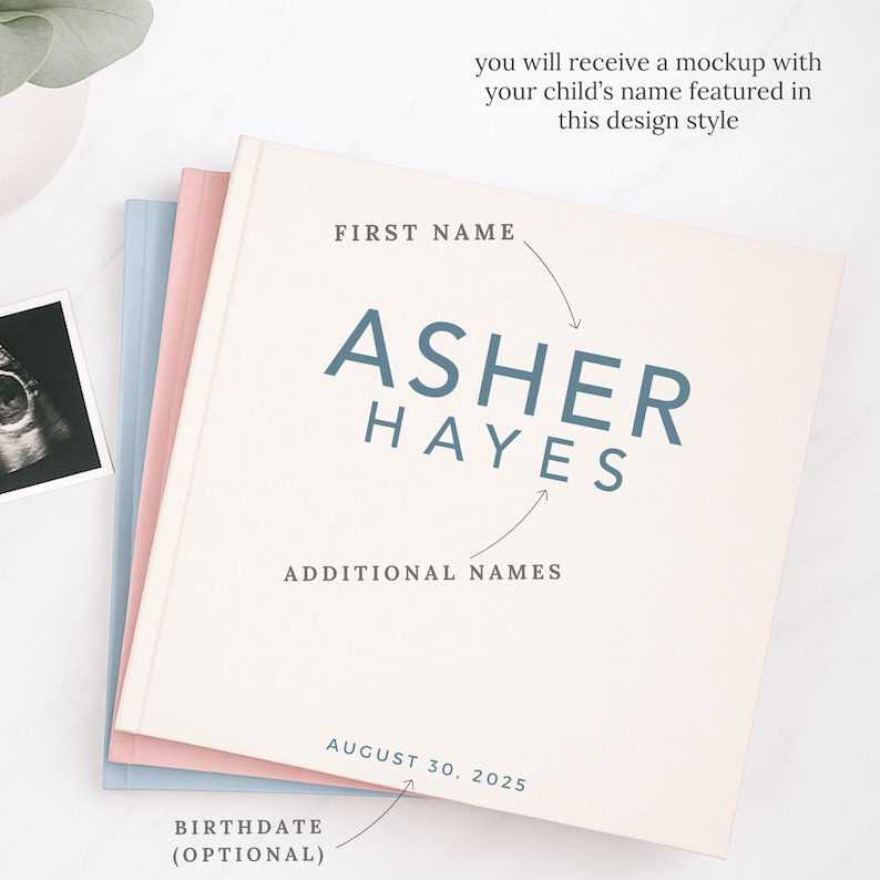May include: A stack of baby memory books in pastel colors. The top book is cream-colored with the name "Asher Hayes" in blue lettering. Text on the cover indicates space for first and additional names, and birthdate. The text "you will receive a mockup with your child's name featured in this design style" is also visible.