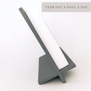 K&ouml;nnte beinhalten: Ein grauer Holz-Staffelei-St&auml;nder mit einem wei&szlig;en Blattkalender. Der Kalender hat den Text "TEAR OFF A PAGE A DAY" oben aufgedruckt.