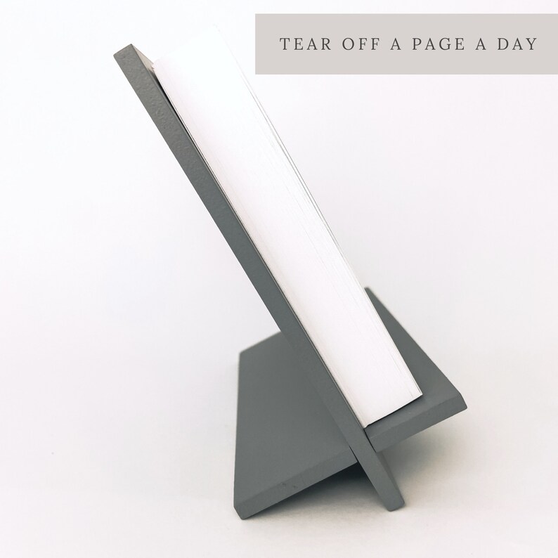 K&ouml;nnte beinhalten: Ein grauer Holz-Staffelei-St&auml;nder mit einem wei&szlig;en Blattkalender. Der Kalender hat den Text "TEAR OFF A PAGE A DAY" oben aufgedruckt.