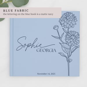 May include: A pale blue book featuring the name "Sophie" and the word "Georgia" in navy script. A floral illustration is on the right. The date "November 14, 2025" is at the bottom. The text "BLUE FABRIC" is at the top.