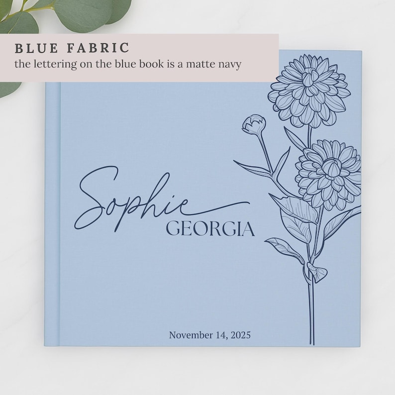May include: A pale blue book featuring the name "Sophie" and the word "Georgia" in navy script. A floral illustration is on the right. The date "November 14, 2025" is at the bottom. The text "BLUE FABRIC" is at the top.