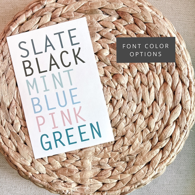 May include: A white card displays color options: Slate, Black, Mint, Blue, Pink, and Green. The text "FONT COLOR OPTIONS" is in a dark gray box. The card rests on a woven, light brown surface.