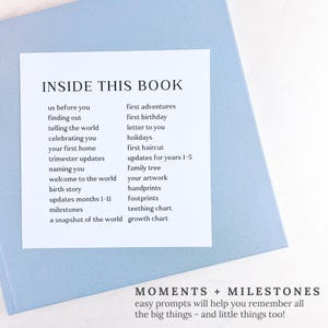 May include: A pale blue book with a white insert listing prompts like "us before you", "first birthday", and "milestones". The text "INSIDE THIS BOOK" is at the top. The bottom reads "MOMENTS + MILESTONES".