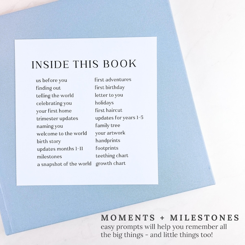 May include: A pale blue book with a white insert listing prompts like "us before you", "first birthday", and "milestones". The text "INSIDE THIS BOOK" is at the top. The bottom reads "MOMENTS + MILESTONES".