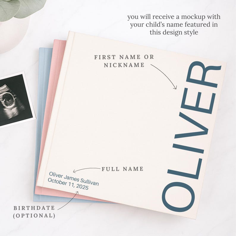 May include: A stack of three baby memory books in pastel colors. The top book is off-white with the name "OLIVER" in large, dark blue letters. Text on the book includes "FIRST NAME OR NICKNAME" and "FULL NAME". An ultrasound photo is visible.