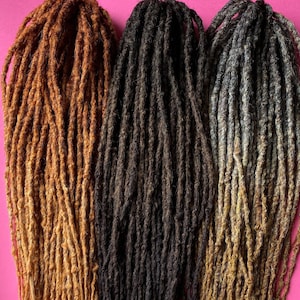 May include: Three sets of dreadlocks in varying shades of brown and blonde, arranged against a bright pink background. The dreadlocks are long and textured, with a natural appearance. The colors range from light blonde to dark brown.