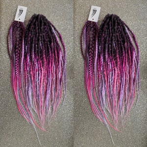 May include: Two sets of long, ombre synthetic dreadlocks in shades of pink, purple, and black. The dreadlocks are arranged in a fan shape and are ready to be installed.