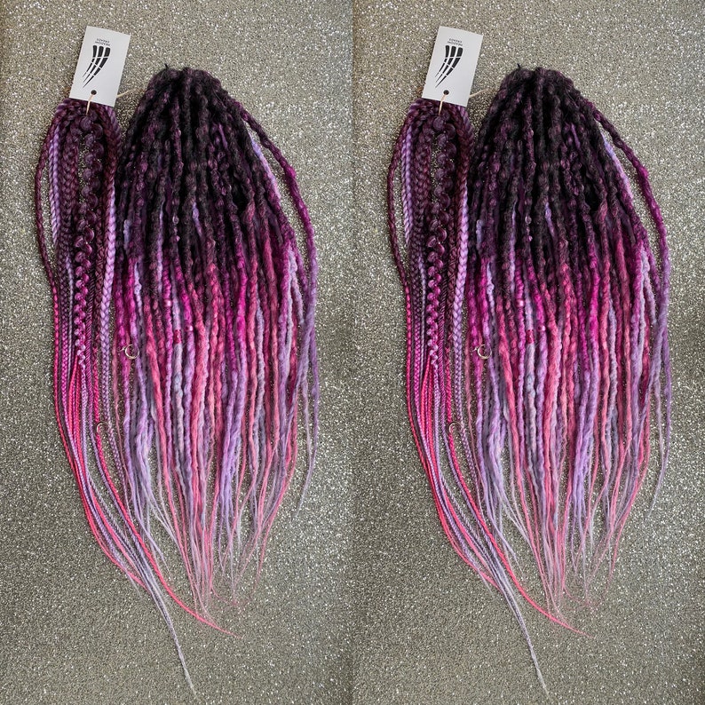 May include: Two sets of long, ombre synthetic dreadlocks in shades of pink, purple, and black. The dreadlocks are arranged in a fan shape and are ready to be installed.