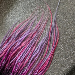 May include: A collection of pink and purple ombre hair extensions. The extensions are made of synthetic hair and are ready to be added to your hair.