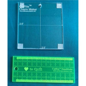 May include: A clear plastic quilting ruler with the text "CutRite™ Charm Maker" and "www.quiltersparadiseesc.com". The ruler is divided into 2.5 inch squares. A green ruler with the text "CutRite™ HandiRuler" and "www.quiltersparadiseesc.com" is below the clear ruler.