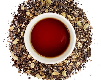 May include: A cup of red tea surrounded by loose leaf black tea and spices, including ginger, cardamom, and cinnamon.