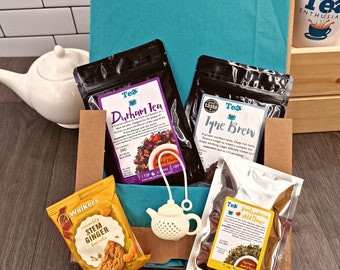 May include: A teal blue gift box filled with tea and biscuits. The box contains three different types of tea: Durham Tea, Tyne Brew, and Northumbrian Wild Flower. The box also includes a package of crumbly stem ginger biscuits. The box is decorated with a white teacup and a white tea infuser.