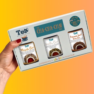May include: A white box with a teal border and the text "The Tea Enthusiasts CHA-CHA-CHAI Box" on the front. The box contains three glass jars of loose leaf tea: Masala Chai, Vanilla Chai, and Cinnamon Swirl Rooibos Chai. The box is labeled "Loose leaf tea VARIETY PACK".