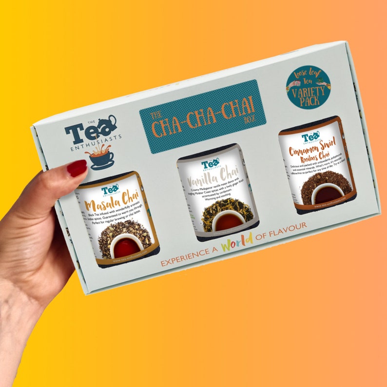 May include: A white box with a teal border and the text "The Tea Enthusiasts CHA-CHA-CHAI Box" on the front. The box contains three glass jars of loose leaf tea: Masala Chai, Vanilla Chai, and Cinnamon Swirl Rooibos Chai. The box is labeled "Loose leaf tea VARIETY PACK".