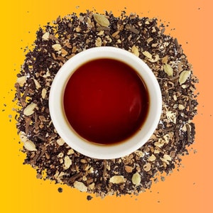 May include: A white ceramic cup filled with a dark red tea, surrounded by a mixture of dried tea leaves, spices, and herbs.