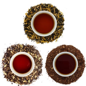 May include: Three white teacups filled with dark red tea, each surrounded by a different type of loose leaf tea. The teacups are on a white background.