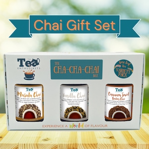 May include: A white gift box with a teal border and the text "Chai Gift Set" on the front. The box contains three glass jars of loose leaf tea: Masala Chai, Vanilla Chai, and Cinnamon Swirl Rooibos Chai. The text "THE CHA-CHA-CHAI BOX" is printed on the front of the box.