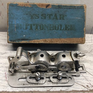 May include: A vintage silver-toned buttonhole attachment for a sewing machine. The attachment has a lever, two dials, and a cutting blade. The box is blue with the words "Y.S. STAR BUTTONHOLE" printed on it.