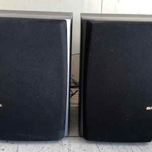 以下が含まれることがあります： 銀色のトリムが付いた黒い Aiwa スピーカーのペア。スピーカーは長方形で、黒い布製のグリルが付いています。