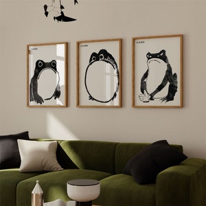 Peut inclure: Trois impressions encadrées en noir et blanc de grenouilles sur un mur blanc. Les impressions sont toutes de la même taille et ont un design simple et minimaliste. Les grenouilles sont représentées dans différentes poses, avec une grenouille assise sur un nénuphar, une autre grenouille nageant dans un étang et la troisième grenouille sautant en l'air.
