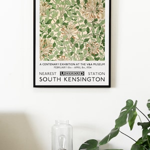 May include: A black and white poster with the text "WILLIAM MORRIS" at the top. The poster features a floral design with green leaves and orange flowers. The text "A CENTENARY EXHIBITION AT THE V&A MUSEUM FEBRUARY 10th - APRIL 8th, 1934 NEAREST UNDERGROUND STATION SOUTH KENSINGTON" is at the bottom of the poster.