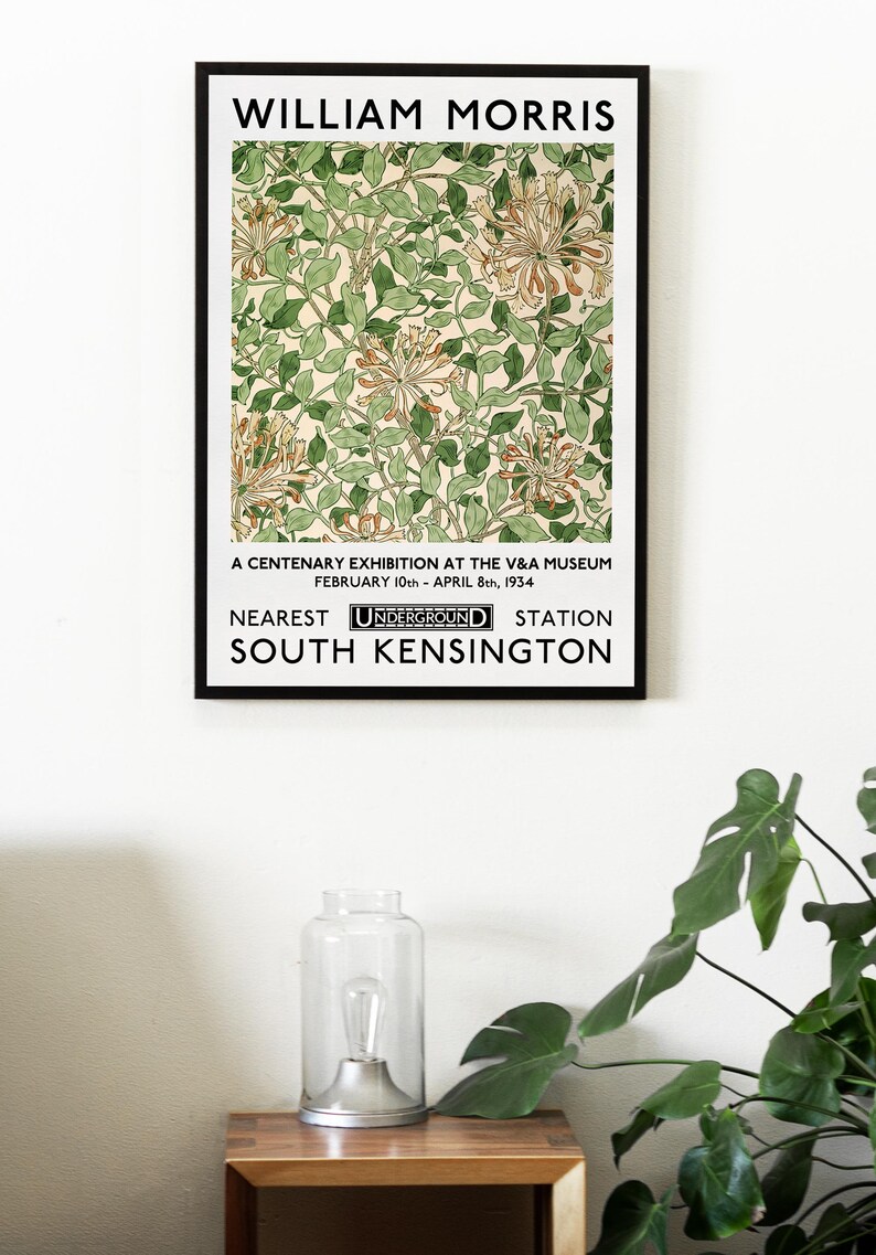 May include: A black and white poster with the text "WILLIAM MORRIS" at the top. The poster features a floral design with green leaves and orange flowers. The text "A CENTENARY EXHIBITION AT THE V&A MUSEUM FEBRUARY 10th - APRIL 8th, 1934 NEAREST UNDERGROUND STATION SOUTH KENSINGTON" is at the bottom of the poster.