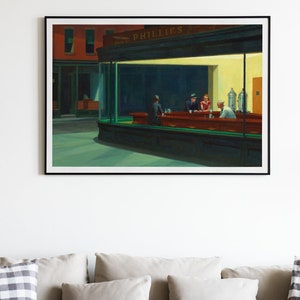 May include: Framed print of Edward Hopper's "Nighthawks" painting. The artwork depicts a diner at night with three patrons and a server. The diner is brightly lit, contrasting with the dark street outside. The print is displayed above a sofa.