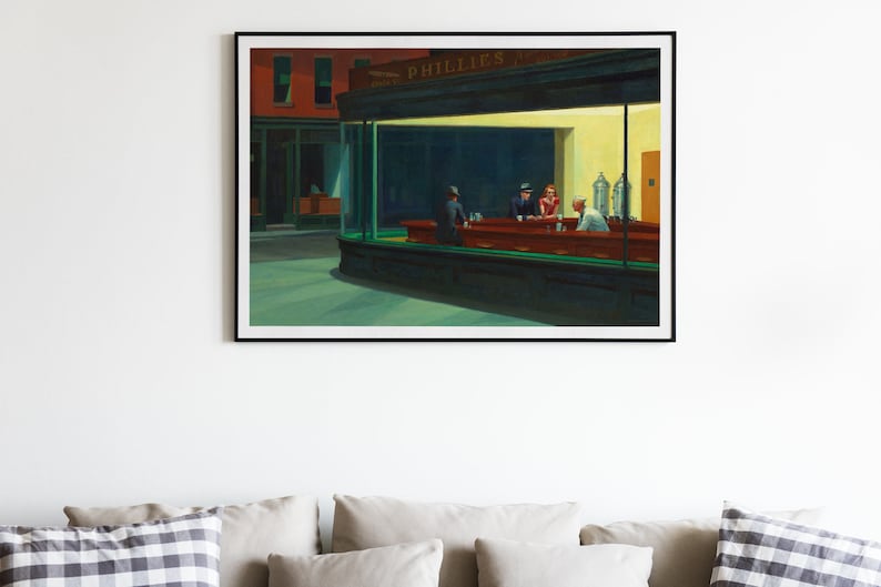 May include: Framed print of Edward Hopper's "Nighthawks" painting. The artwork depicts a diner at night with three patrons and a server. The diner is brightly lit, contrasting with the dark street outside. The print is displayed above a sofa.