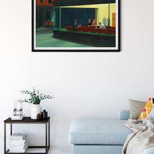 May include: A framed print of Edward Hopper's "Nighthawks" painting. The artwork depicts a diner scene with figures at the counter, bathed in the glow of artificial light. The diner is set on a street corner, with the word "PHILLIES" visible on the awning.