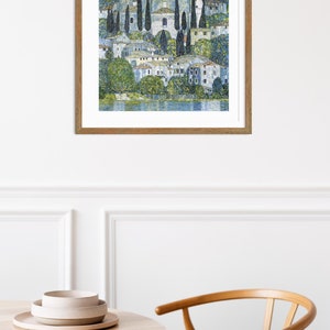 Puede incluir: Una pintura enmarcada de un peque&ntilde;o pueblo en un lago. El pueblo est&aacute; formado por edificios blancos con &aacute;rboles verdes y un cielo azul. La pintura est&aacute; hecha en un estilo de mosaico.