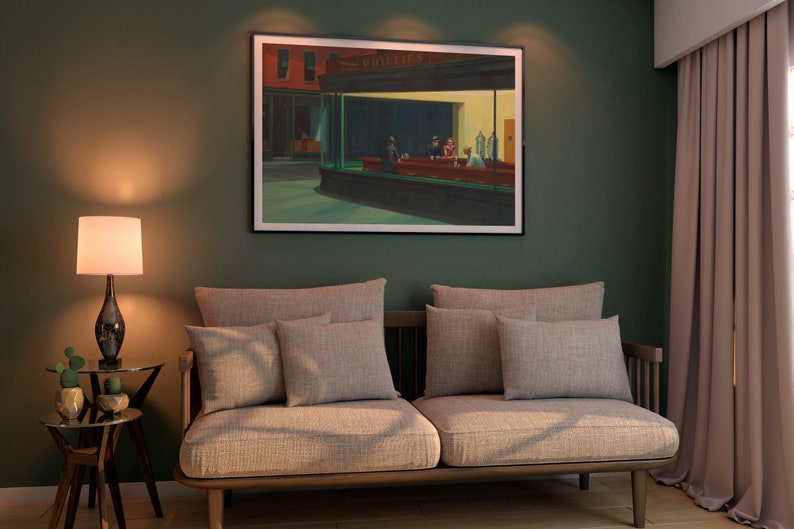 May include: A living room scene featuring a framed print of Edward Hopper's "Nighthawks" painting. The artwork hangs above a light gray sofa with matching pillows. A lamp with a white shade and a small side table with decorative plants complete the decor.