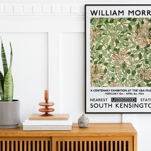 May include: A black and white poster with the text "WILLIAM MORRIS" at the top. The poster features a floral pattern with green leaves and white flowers. The text below the image reads "A CENTENARY EXHIBITION AT THE V&A MUSEUM FEBRUARY 10th - APRIL 8th, 1934 NEAREST UNDERGROUND STATION SOUTH KENSINGTON."