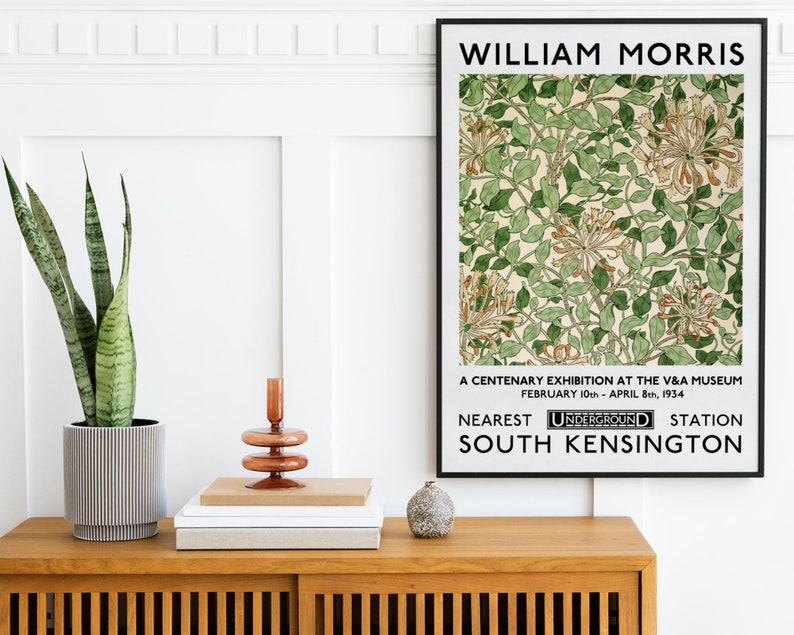May include: A black and white poster with the text "WILLIAM MORRIS" at the top. The poster features a floral pattern with green leaves and white flowers. The text below the image reads "A CENTENARY EXHIBITION AT THE V&A MUSEUM FEBRUARY 10th - APRIL 8th, 1934 NEAREST UNDERGROUND STATION SOUTH KENSINGTON."