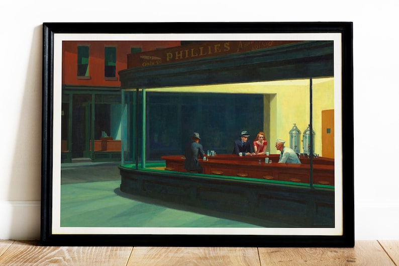 May include: Framed print of Edward Hopper's "Nighthawks" painting. The artwork depicts a late-night diner scene with three patrons and a server. The diner is brightly lit, contrasting with the dark street outside. The frame is black.