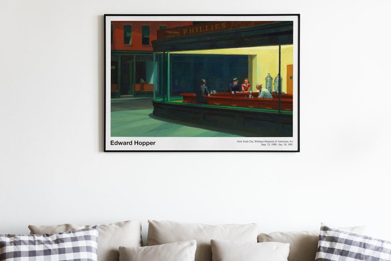 May include: A painting by Edward Hopper titled "Nighthawks" depicting a diner at night with three customers and a server. The diner is brightly lit with a yellow glow, while the street outside is dark. The painting is framed in black.