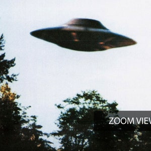 May include: A black flying saucer shaped object against a white cloudy sky. The object is flying over a forest of green trees. The text "ZOOM VIEW" is in the bottom right corner of the image.