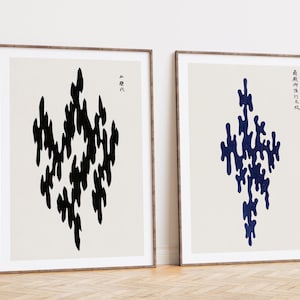 Puede incluir: Dos impresiones enmarcadas con diseños abstractos en negro y azul. Las impresiones están sobre un fondo blanco y tienen texto japonés en la esquina superior derecha. El texto de la impresión de la izquierda dice "黑" y el texto de la impresión de la derecha dice "黒神乃水衣".