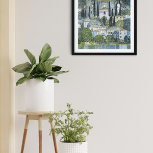 Puede incluir: Una pintura enmarcada que representa una escena de pueblo con una iglesia, &aacute;rboles y un lago. La pintura est&aacute; realizada en estilo puntillista, con peque&ntilde;os puntos de color que crean la imagen.