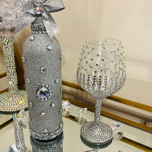 May include: A silver glitter wine bottle with a rhinestone bow and a silver glitter wine glass with rhinestones.
