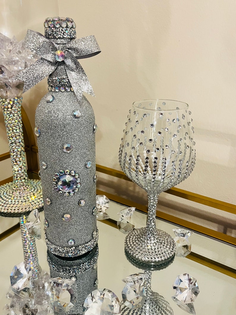 May include: A silver glitter wine bottle with a rhinestone bow and a silver glitter wine glass with rhinestones.