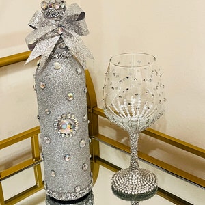 May include: A silver glitter wine bottle with a silver glitter bow and a silver glitter wine glass with rhinestones.