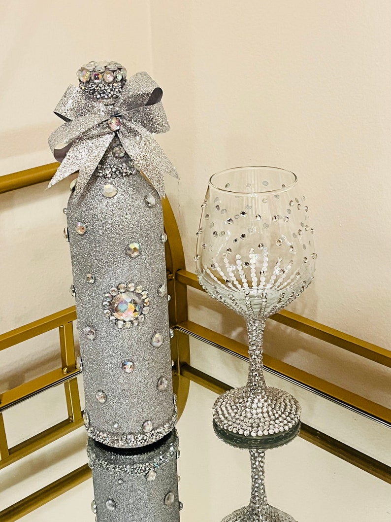 May include: A silver glitter wine bottle with a silver glitter bow and a silver glitter wine glass with rhinestones.