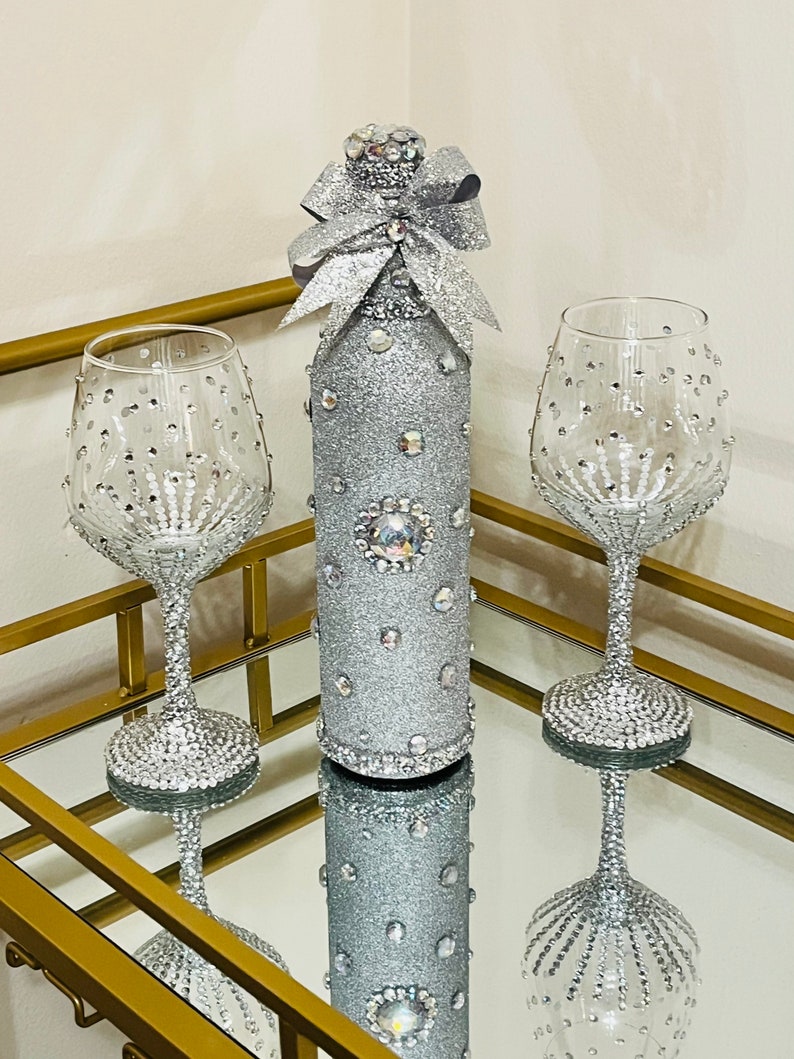 May include: A silver glitter wine bottle with a silver glitter bow and two silver glitter wine glasses on a gold tray.