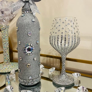 May include: A silver glitter wine bottle with a silver bow and rhinestones, and a silver glitter wine glass with rhinestones.